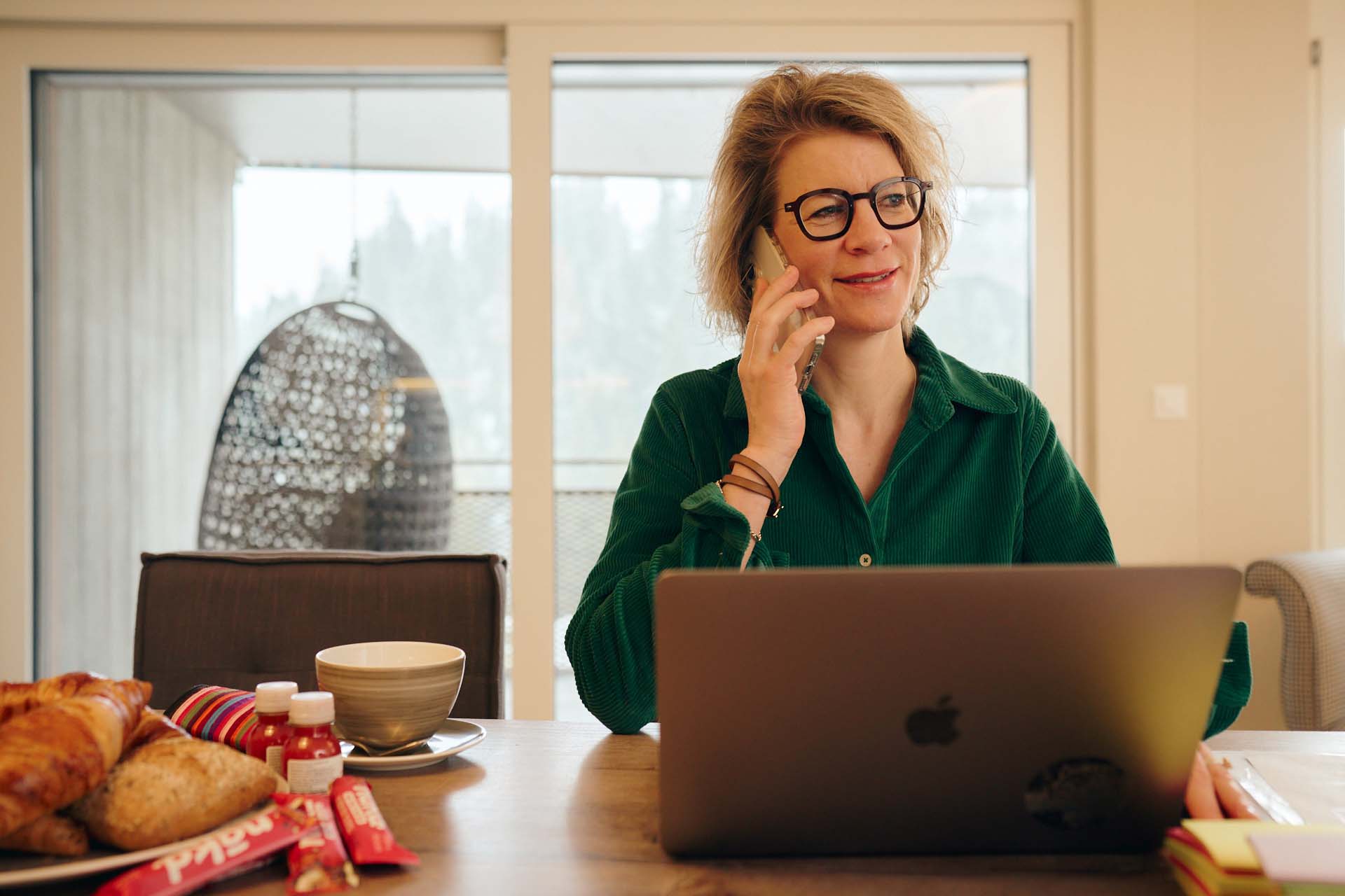 Nicoletta, in dunkelgrünem Outfit, arbeitet entspannt an ihrem Laptop. Sie lacht.