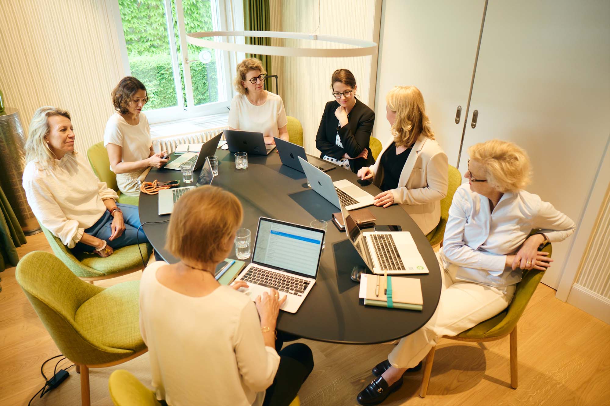 Nicoletta Müller und ihr Team an einem ovalen Konferenztisch im Hotel Alma. Gespannt hören die sechs Frauen Stephanie zu. Isabelle macht Notizen auf ihrem Laptop.